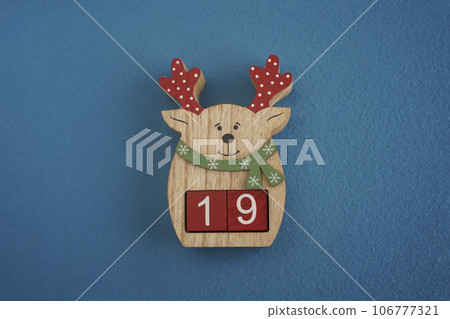 Festive wooden deer with Viva Magenta cubes 19 on blue background close-up top view. Christmas concept of date or time 106777321