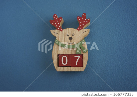 Festive wooden deer with Viva Magenta cubes 07 on blue background close-up top view. Christmas concept of date or time 106777333