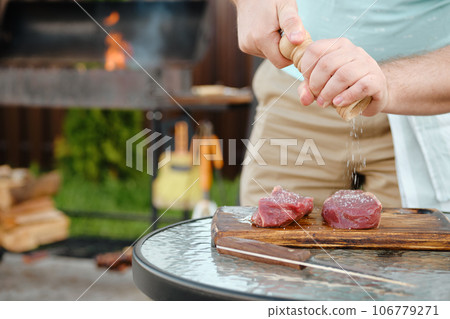 Man using hand mill to season raw strip steak with salt 106779271
