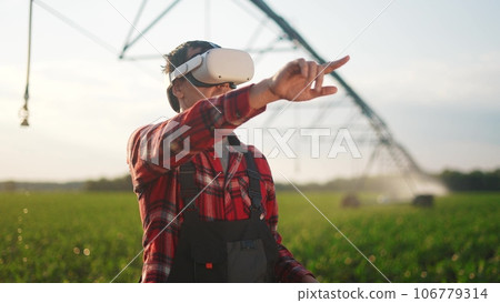 agriculture virtual reality. a farmer in virtual reality glasses controls a machine to irrigate corn field. agriculture virtual reality concept. business a farmer vr in works in field with corn 106779314