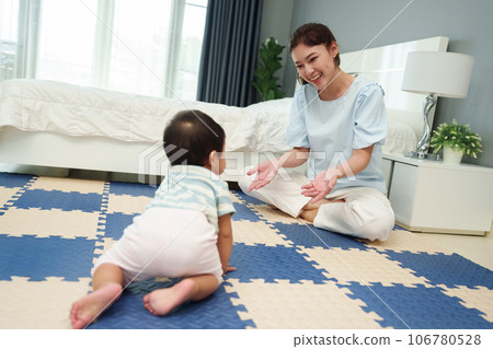 happy mother watching her infant baby crawlinf on play mat or jigsa floor in bedroom 106780528