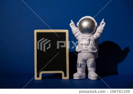 Plastic toy astronaut with blackboard template mock up for your text on colorful blue background Copy space. Concept of out of earth travel, private spaceman commercial flights missions and 106781109