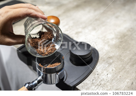 Barista hand pouring fresh ground coffee into the portafilter 106783224