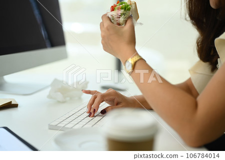 Cropped shot of female office worker sitting at desk and eating sandwich for lunch 106784014