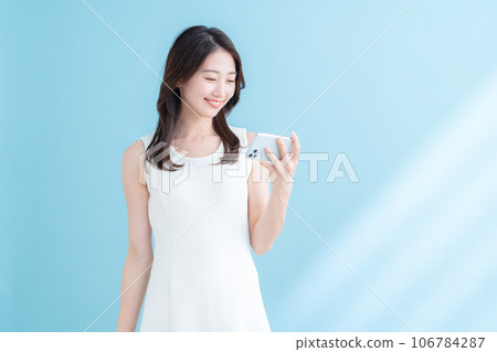 A young woman operating a smartphone on a blue background where the sun shines 106784287