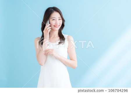 A young woman operating a smartphone on a blue background where the sun shines 106784296