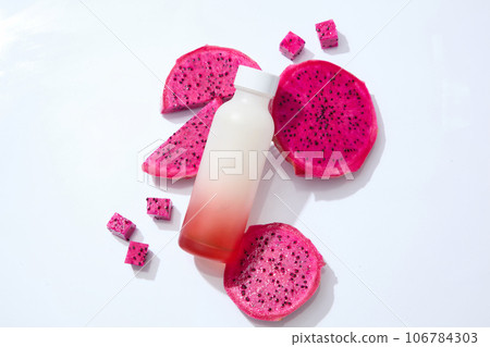 Top view of red dragon fruit decorated with a bottle without label. White background. Dragon fruit (Hylocereus) is an exotic fruit that is high in fiber Top view of red dragon fruit decorated with a bottle without label. White background. Dragon fruit (Hylocereus) is an exotic fruit that is high in fiber 106784303