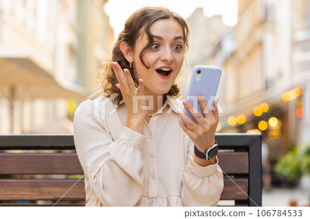 Amazed woman use smartphone celebrating win good message news lottery jackpot victory in city street 106784533