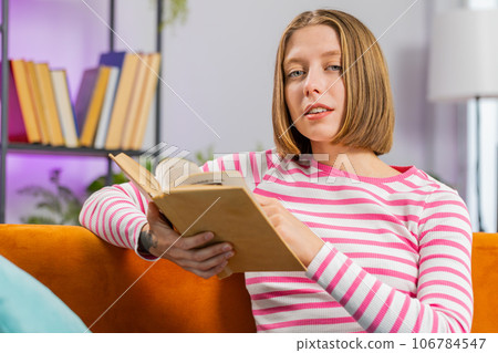 Young woman relaxing interesting book turning pages smiling enjoying literature taking rest on sofa 106784547