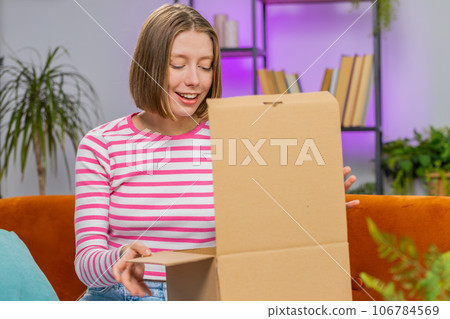 Happy young woman shopper unpacking cardboard box delivery parcel online shopping purchase at home Happy young woman shopper unpacking cardboard box delivery parcel online shopping purchase at home 106784569