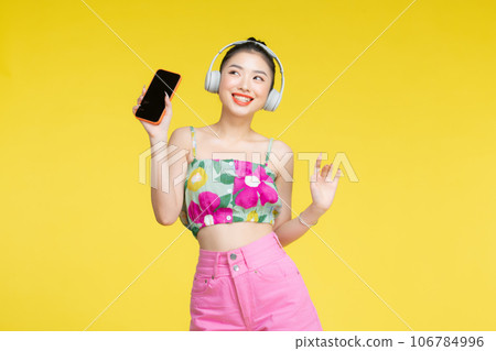 Happy cheerful Asian woman wearing wireless headphones listening to music from smartphone Happy cheerful Asian woman wearing wireless headphones listening to music from smartphone 106784996