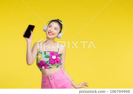 Young Asian woman wearing headphones dancing and listening to music from smartphone Young Asian woman wearing headphones dancing and listening to music from smartphone 106784998