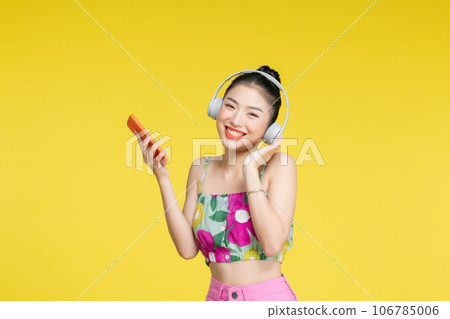 Happy cheerful Asian woman wearing wireless headphones listening to music from smartphone Happy cheerful Asian woman wearing wireless headphones listening to music from smartphone 106785006