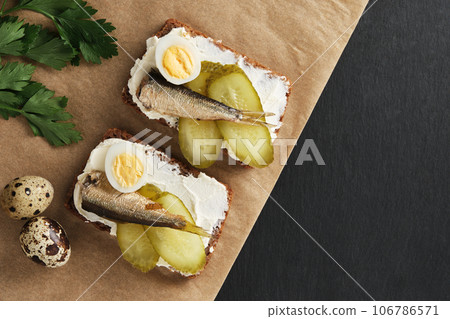 Sandwiches with sprats, quail eggs, pickles on wooden serving tray on black stone background. Appetiser, seafood, flat lay 106786571