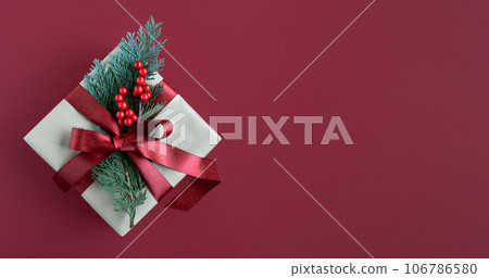 Craft gift box with red ribbon, thuja sprig and berries on red background. Place for your text. Craft gift box with red ribbon, thuja sprig and berries on red background. Place for your text. 106786580