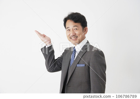 Middle-aged businessman pointing to the left side with the palm of his hand, white background 106786789