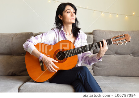 45 y.o. Russian woman playing guitar, sitting on a sofa at home. 45 y.o. Russian woman playing guitar, sitting on a sofa at home. 106787084