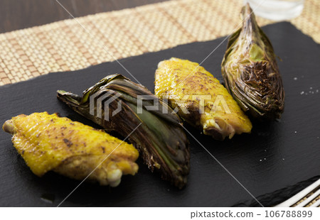 Cooked fried chicken wings and halves artichokes on black stone plate 106788899
