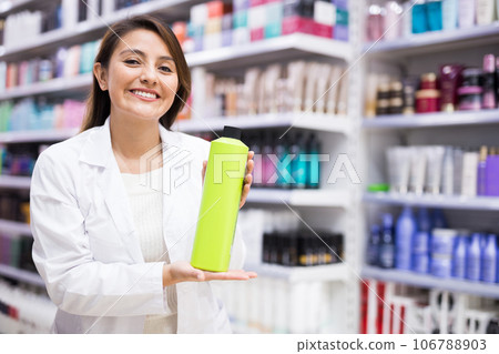 Cheerful saleswoman offering hair care products in cosmetic shop Cheerful saleswoman offering hair care products in cosmetic shop 106788903