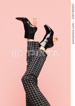 Female legs in black heeled boots, in checkered pants over pink background. Smart casual, business style Female legs in black heeled boots, in checkered pants over pink background. Smart casual, business style 106790897