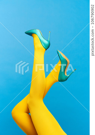 Female slender legs wearing stylish, heeled, green shoes and yellow tights over blue background Female slender legs wearing stylish, heeled, green shoes and yellow tights over blue background 106790902