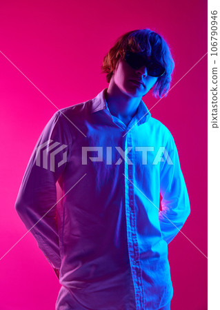 Portrait of young man, student in white shirt and sungllasses posing against pink studio background in neon lights Portrait of young man, student in white shirt and sungllasses posing against pink studio background in neon lights 106790946