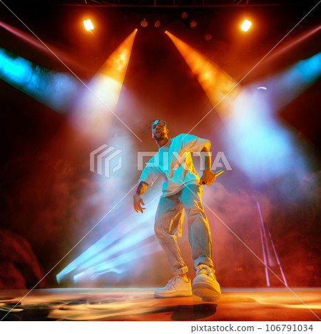 Rap musician. Young artistic man with dreads performing on stage over multicolored neon lights. Concert at night club Rap musician. Young artistic man with dreads performing on stage over multicolored neon lights. Concert at night club 106791034