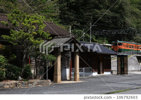 A tangerine-colored train (115 series) arriving at a rural station 106792603