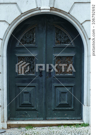 Beautiful big old ancient blue wooden arched door of stone building house decorated with forgings carvings ornaments. Beautiful big old ancient blue wooden arched door of stone building house decorated with forgings carvings ornaments. 106792692
