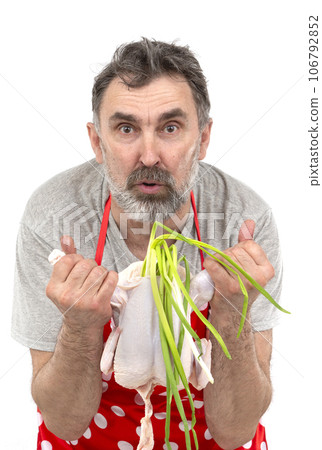 An elderly bearded male cook in a red polka-dot apron holds a raw chicken and a bunch of onions on a white background. Cook with chicken. An elderly bearded male cook in a red polka-dot apron holds a raw chicken and a bunch of onions on a white background. Cook with chicken. 106792852