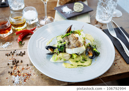 Cod fillet with cauliflower cream, asparagus, clam-wine sauce and mussles. Delicious seafood fish closeup served on a table for lunch in modern cuisine gourmet restaurant Cod fillet with cauliflower cream, asparagus, clam-wine sauce and mussles. Delicious seafood fish closeup served on a table for lunch in modern cuisine gourmet restaurant 106792994