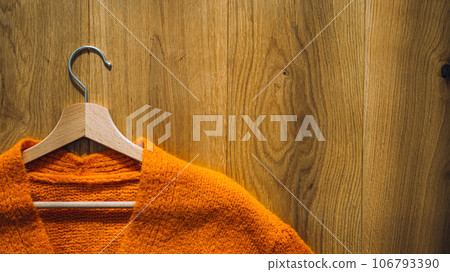 Autumn fall minimalist wardrobe with orange warm knitted sweater on wooden clothes hanger. Autumn capsule, warm fashion trends and stylish warm background, knitwear, copy space. 106793390