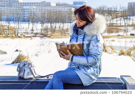 Young woman sitting on the bench, writing in the notebook and smiling on a winter day 106794020
