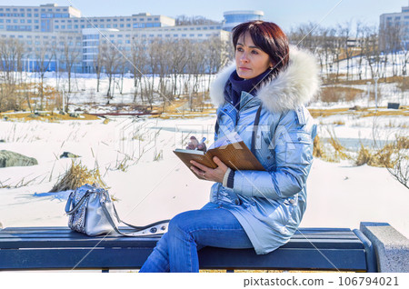 Young woman sitting on the bench, writing in the notebook and smiling on a winter day 106794021