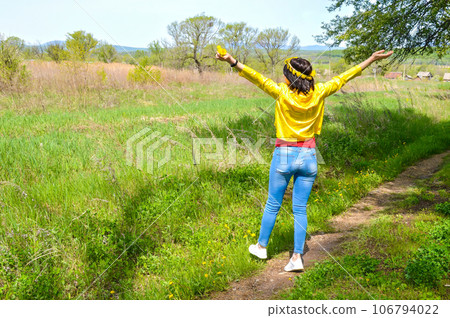 Brunette woman with bouquet of dandelions and wreath embracing nature with open arms in countryside. copy space 106794022