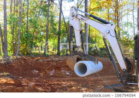 Underground installation prep worker employs tractor to lift concrete a sewage pipes Underground installation prep worker employs tractor to lift concrete a sewage pipes 106794094