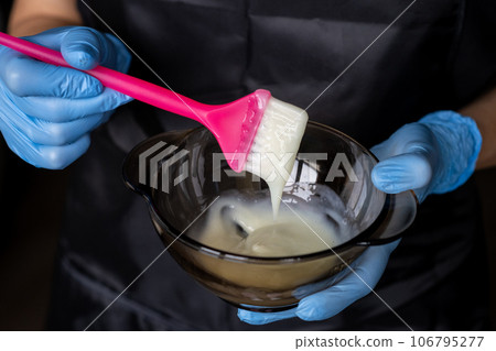girl in blue rubber protective gloves holding a brush in her hands and stirring hair dye close-up colorist hair care at home hair mask.  106795277