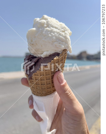 hand holds ice cream cone over sea in a sunny day 106797233