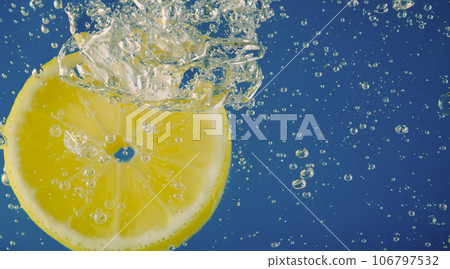 Underwater lemon slice in soda water or lemonade with bubbles. Refreshing soda tonic fizzy cocktail. Close up of lemons and ice cubes in glass. Lime in splashing sparkling water cold drink beverage. 106797532