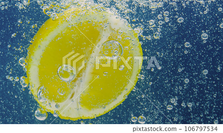 Underwater lemon slice in soda water or lemonade with bubbles. Refreshing soda tonic fizzy cocktail. Close up of lemons and ice cubes in glass. Lime in splashing sparkling water cold drink beverage. 106797534