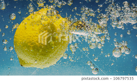 Underwater lemon slice in soda water or lemonade with bubbles. Refreshing soda tonic fizzy cocktail. Close up of lemons and ice cubes in glass. Lime in splashing sparkling water cold drink beverage. 106797535