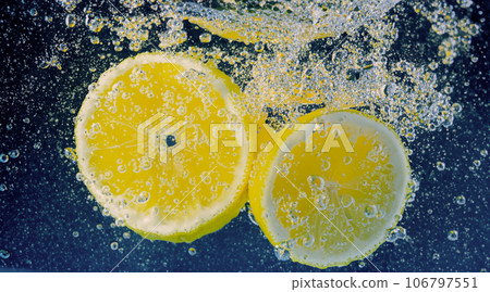 Underwater lemon slice in soda water or lemonade with bubbles. Refreshing soda tonic fizzy cocktail. Close up of lemons and ice cubes in glass. Lime in splashing sparkling water cold drink beverage. 106797551