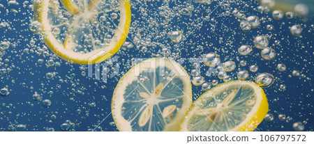 Underwater lemon slice in soda water or lemonade with bubbles. Refreshing soda tonic fizzy cocktail. Close up of lemons and ice cubes in glass. Lime in splashing sparkling water cold drink beverage. 106797572