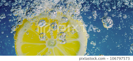 Underwater lemon slice in soda water or lemonade with bubbles. Refreshing soda tonic fizzy cocktail. Close up of lemons and ice cubes in glass. Lime in splashing sparkling water cold drink beverage. Underwater lemon slice in soda water or lemonade with bubbles. Refreshing soda tonic fizzy cocktail. Close up of lemons and ice cubes in glass. Lime in splashing sparkling water cold drink beverage. 106797573