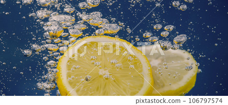 Underwater lemon slice in soda water or lemonade with bubbles. Refreshing soda tonic fizzy cocktail. Close up of lemons and ice cubes in glass. Lime in splashing sparkling water cold drink beverage. Underwater lemon slice in soda water or lemonade with bubbles. Refreshing soda tonic fizzy cocktail. Close up of lemons and ice cubes in glass. Lime in splashing sparkling water cold drink beverage. 106797574