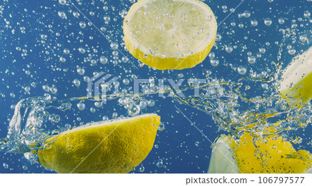 Underwater lemon slice in soda water or lemonade with bubbles. Refreshing soda tonic fizzy cocktail. Close up of lemons and ice cubes in glass. Lime in splashing sparkling water cold drink beverage. 106797577