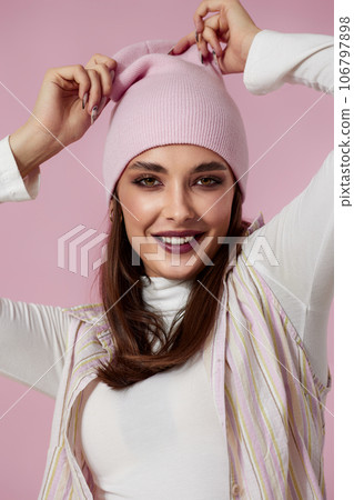 playful woman keeps hands on pink hat on pink background. playful woman keeps hands on pink hat on pink background. 106797898