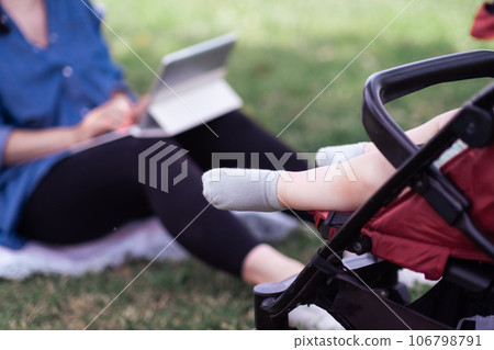 Cute feet in socks of little baby sleeping in buggy near mother working online via tablet computer in summer park healthy child sitting in carriage closeup 106798791