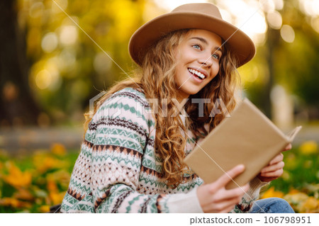 Beautiful curly woman in hat on mat with book in autumn park. Relaxation, solitude with nature. Beautiful curly woman in hat on mat with book in autumn park. Relaxation, solitude with nature. 106798951