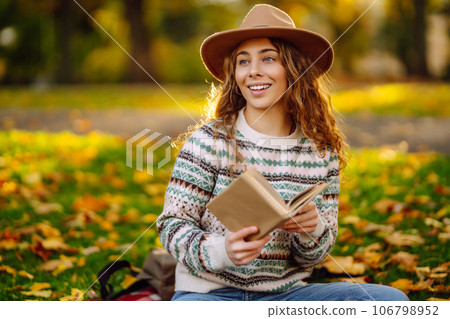 Beautiful curly woman in hat on mat with book in autumn park. Relaxation, solitude with nature. Beautiful curly woman in hat on mat with book in autumn park. Relaxation, solitude with nature. 106798952